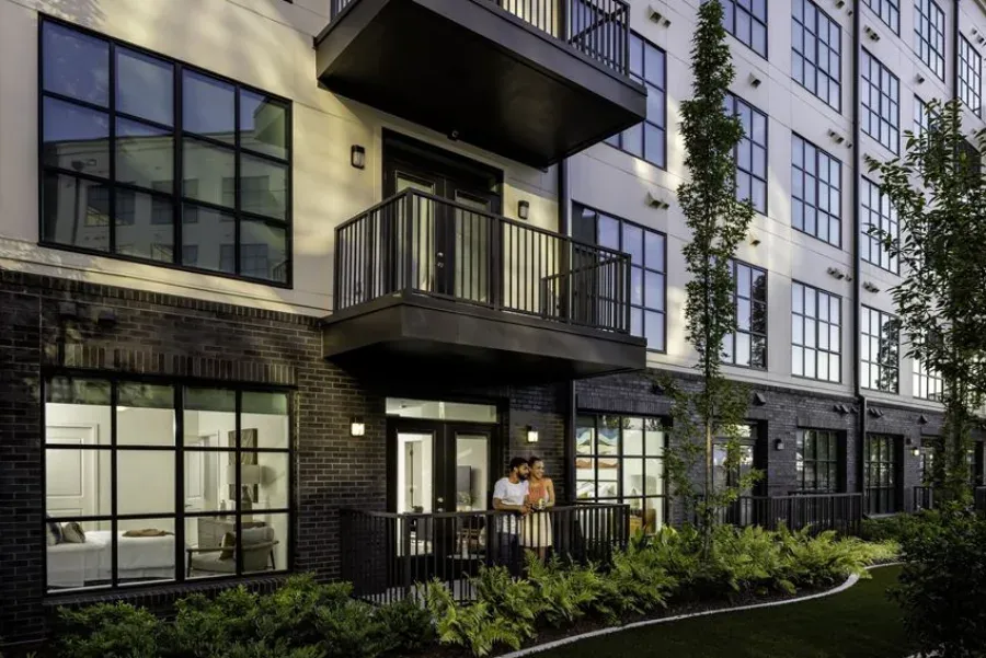 565 Hank in Summerhill at dusk: black-framed windows and a balcony door lit from inside, with residents on a ground-floor patio